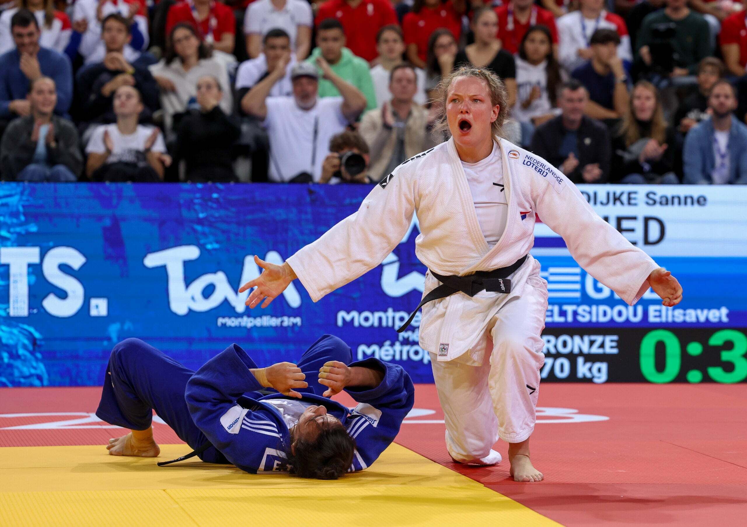 Sanne van Dijke zit op een knie, terwijl haar judo tegenstander in een blauw pak achter haar op de grond ligt. Sanne van Dijke zit op een knie, terwijl haar judo tegenstander in een blauw pak achter haar op de grond ligt.