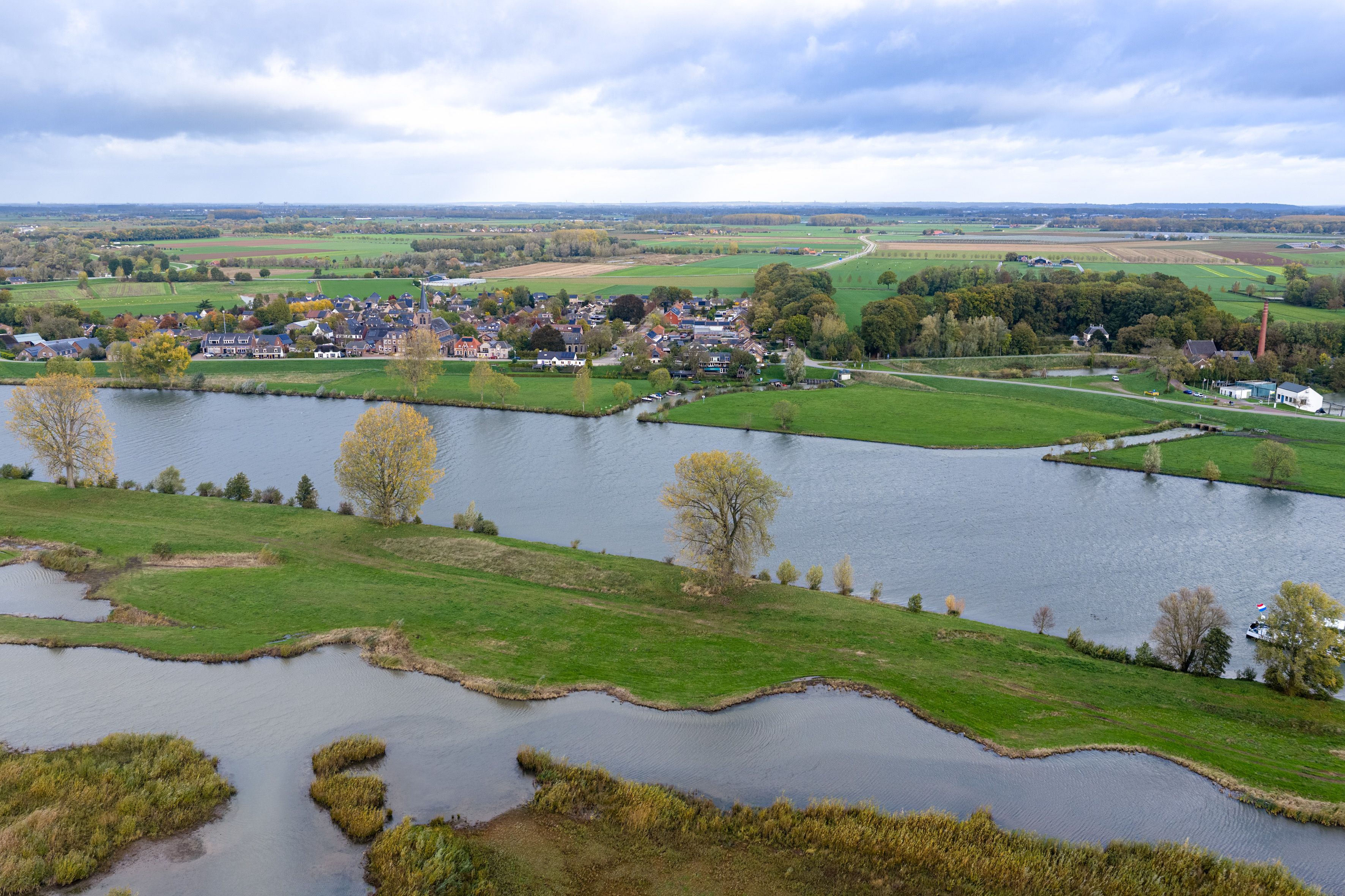 Een rivier vanuit de lucht, met aan de ene kant een klein pittoresk dorp en aan de andere kant volgelopen uiterwaarde Een rivier vanuit de lucht, met aan de ene kant een klein pittoresk dorp en aan de andere kant volgelopen uiterwaarde